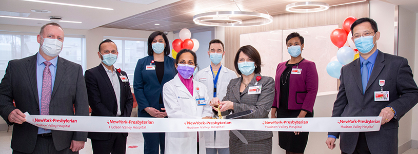 A group of healthcare professionals posing for a photo before cutting a ribbon 