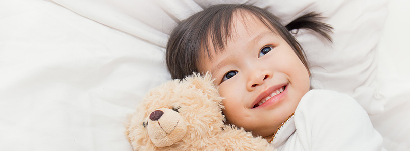 asian child holding stuffed animal in bed