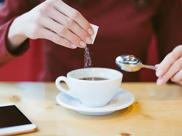 image of person pouring sugar into cup of coffee