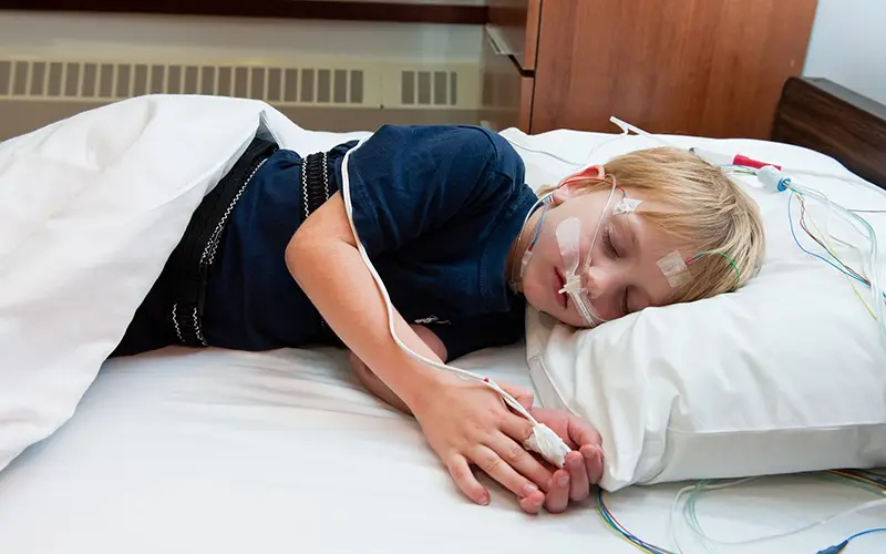 Child sleeping in a bed with white sheets during a polysomnography